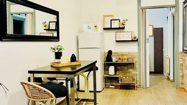 A modern kitchen with a dining area, featuring a wooden table, chairs, a hanging light fixture, and a refrigerator. - Basic Interior Apartment Sagrada Familia (Barcelona)