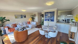 Una sala de estar moderna con sofá, mesa de centro y sillas, un comedor con mesa y sillas, y una cocina con armarios y electrodomésticos.
