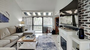 A modern living room with a sofa, coffee table, fireplace, and large windows.