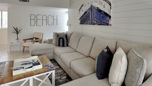 A modern living room with a beige sofa, a wooden coffee table, and a wall-mounted artwork depicting a boat.