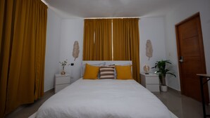 A bedroom with a bed, two nightstands, a potted plant, and a door. -  White Sand Beach Retreat (Punta Cana)