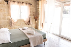 A room with a bed, curtains, a window, and a vase of dried plants.