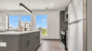 Une cuisine moderne dotée d’un grand îlot central, d’appareils électroménagers en acier inoxydable et offrant une vue sur le paysage urbain grâce à de grandes fenêtres.