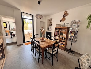 A dining area with a wooden table and chairs, a bookshelf, and a decorative plant.