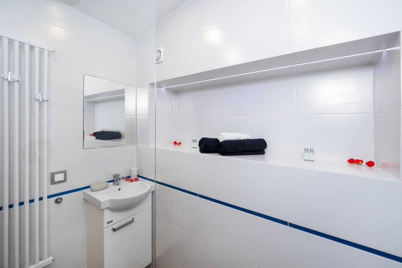 A modern bathroom with a white sink, mirror, and towel rack. There are two towels and a pair of slippers on the shelf.