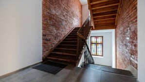 Una escalera de madera con barandilla de metal que conduce a una habitación con ventana y pared de ladrillo.