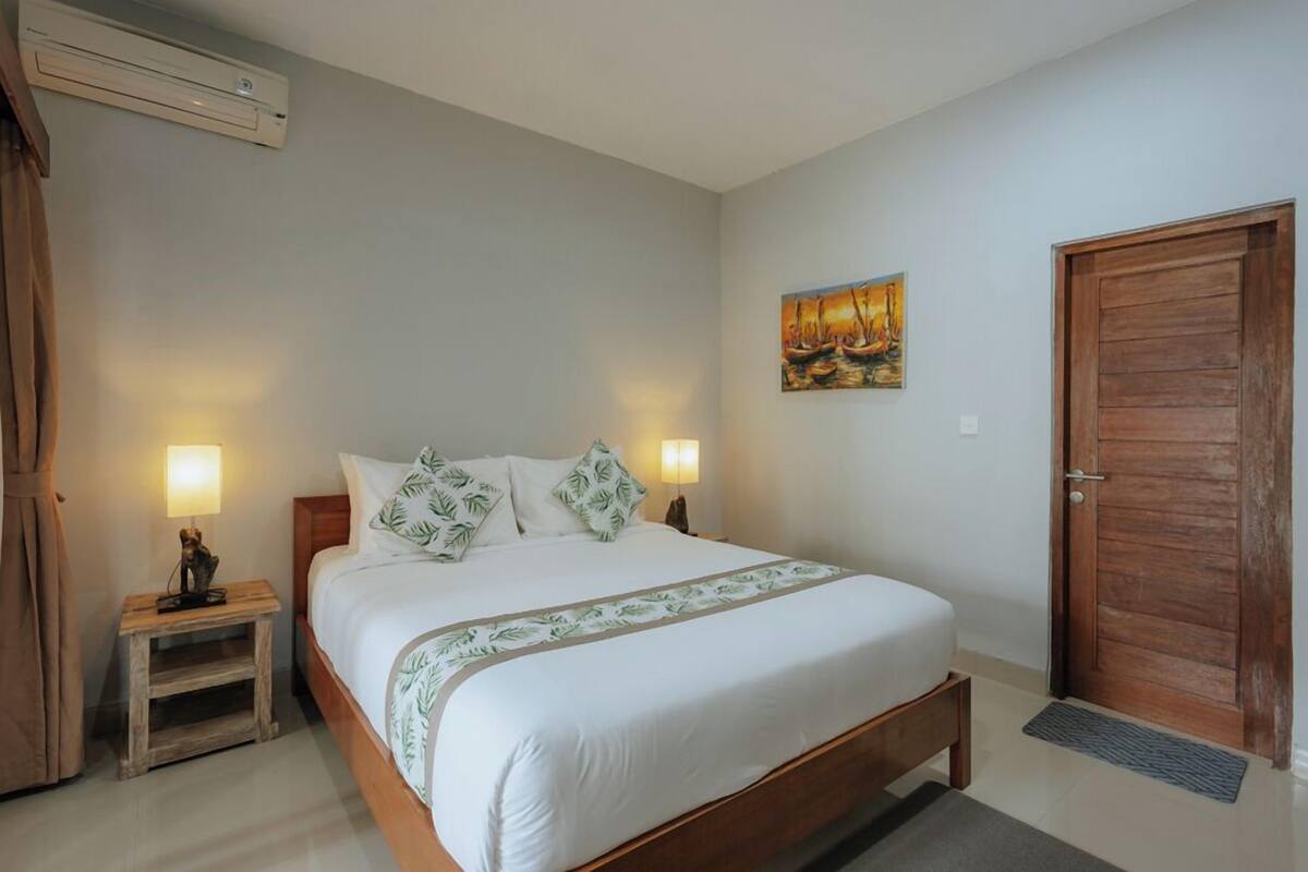Un dormitorio con cama, dos lámparas de noche, un cuadro en la pared y una puerta de madera.