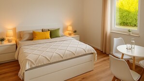Une chambre à coucher bien rangée, avec un lit, des tables de chevet, une petite table avec des chaises et une fenêtre avec des rideaux.