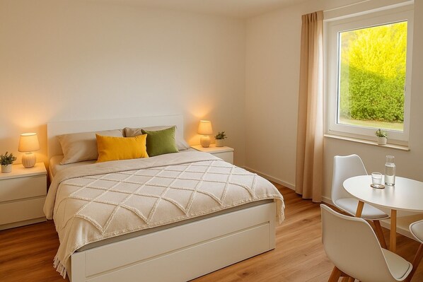 A neatly arranged bedroom with a bed, bedside tables, a small table with chairs, and a window with curtains.