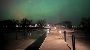 Une jetée en bois s’étendant dans une étendue d’eau, avec des maisons en arrière-plan sous un ciel verdâtre.