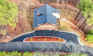 A lodge with a steeply pitched roof, a covered porch, and a landscaped driveway with a flower bed.