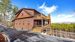 A two-story log cabin with a balcony and a staircase leading to the upper level.
