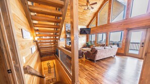A wooden interior with a staircase, a living area with a sofa, and large windows.