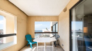 Ein Balkon mit einem weißen Tisch und zwei Stühlen, ein blauer und ein schwarzer, mit Blick auf eine Stadtlandschaft.