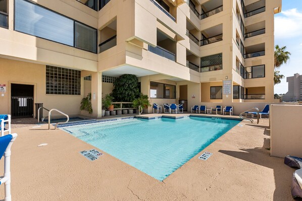 A swimming pool with blue water, surrounded by beige walls and balconies.