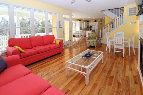 A spacious living room with a red sofa, a glass coffee table, and a staircase leading to a kitchen.