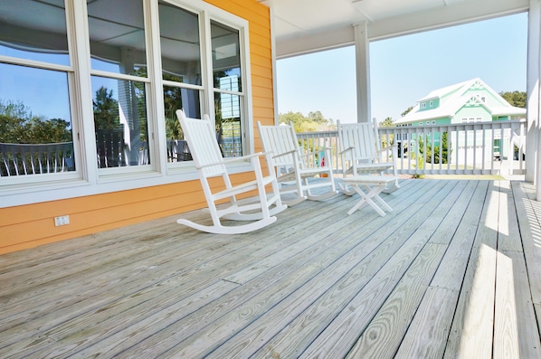 A wooden deck with rocking chairs and a view of a house in the background.