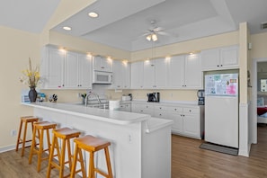 A modern kitchen with white cabinets, a central island with stools, a ceiling fan, and a refrigerator.