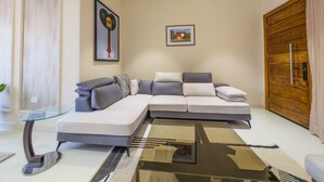A modern living room with a sectional sofa, a glass coffee table, and a wooden door. - Glassvine - 1D (Lagos)