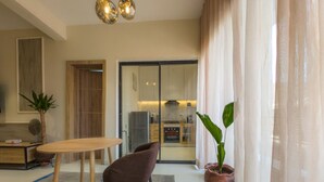 A modern living room with a dining area, a large sliding glass door leading to a kitchen, and a potted plant. - Glassvine - 1D (Lagos)
