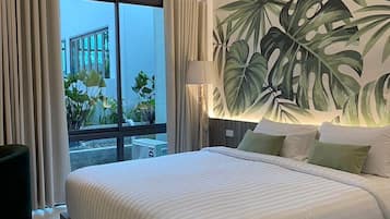 A hotel room with a large bed, a view of the outdoors, and a tropical leaf mural on the wall.