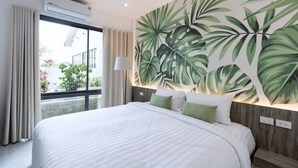 A hotel room with a large bed, a view of the outdoors, a tropical leaf mural, and a window with curtains. - Tree Airport Hotel Hatyai (Khuan Lang)