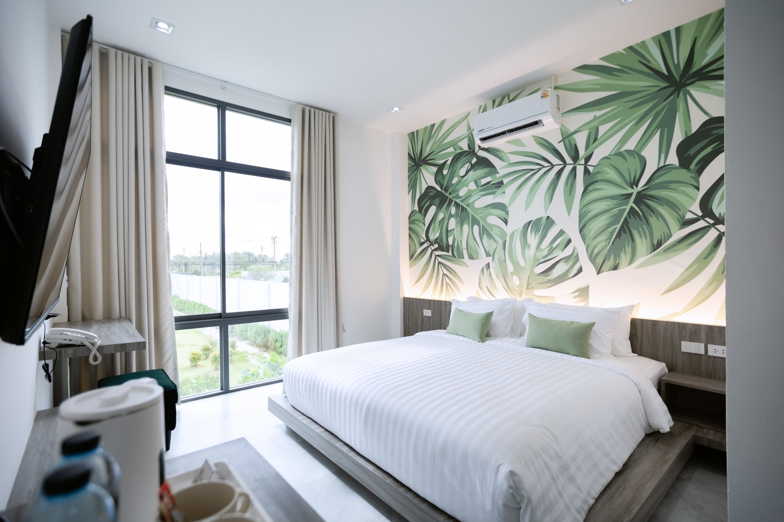 Habitación de hotel con una cama grande, un televisor de pantalla plana montado en la pared, una ventana con cortinas y vistas a zonas verdes.