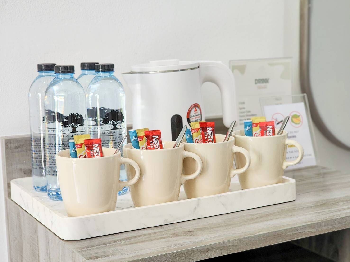 Una bandeja con cuatro tazas, dos botellas de agua y una cafetera sobre una encimera de mármol.