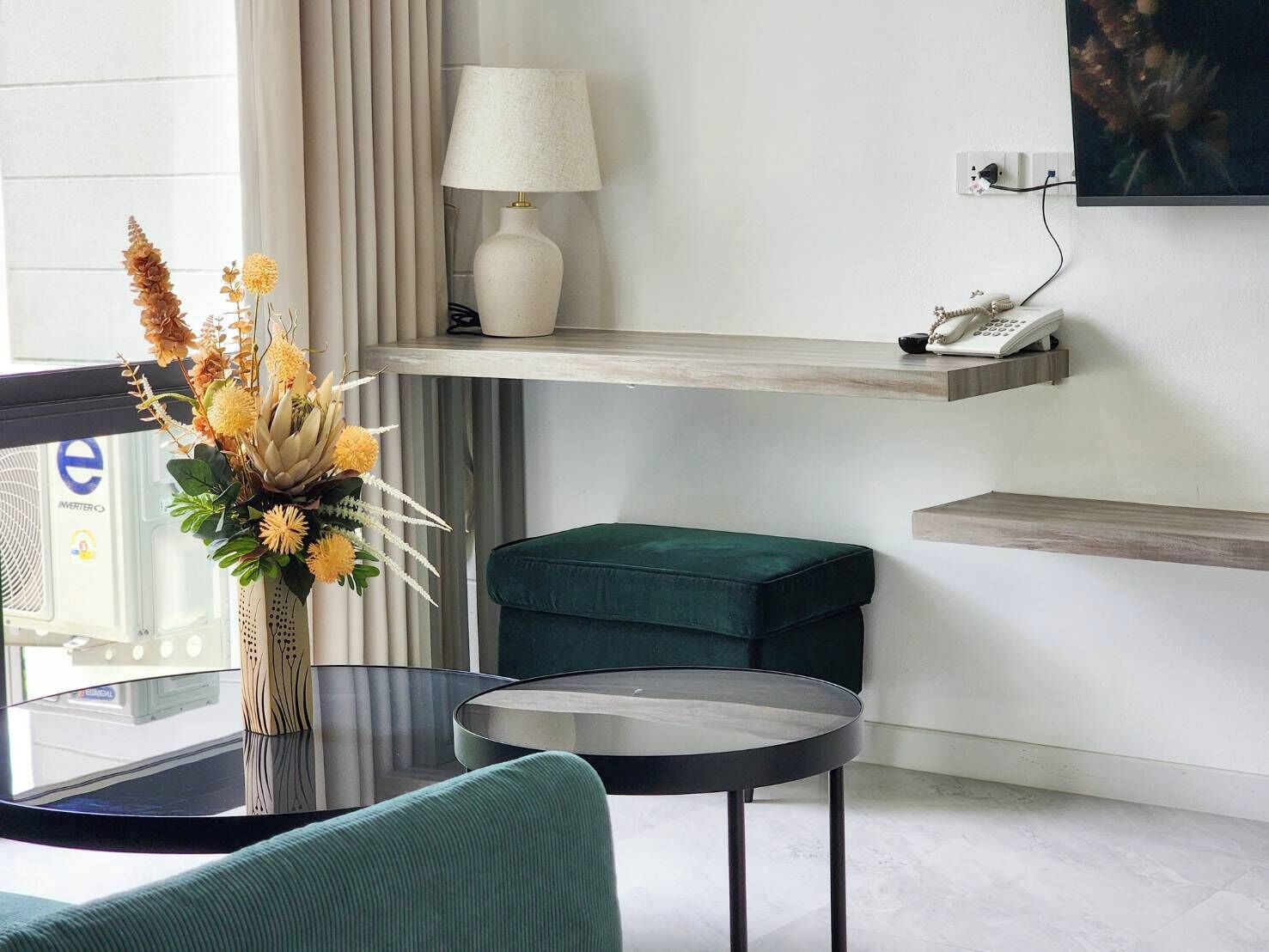 A modern living room with a glass coffee table, a green sofa, a lamp, and a decorative vase with flowers.