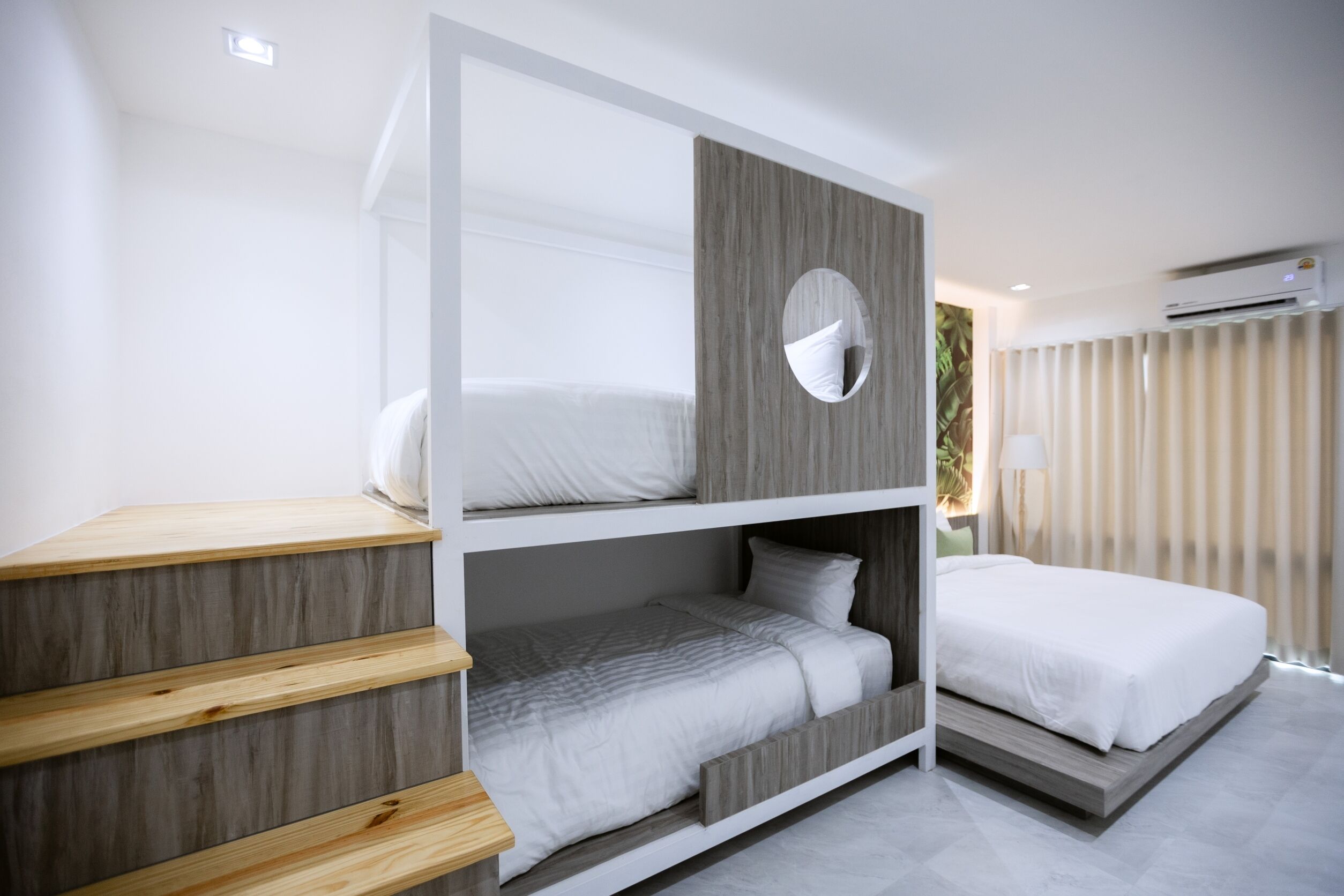 A modern hotel room with a bunk bed, a wooden bench, and a large window with curtains.