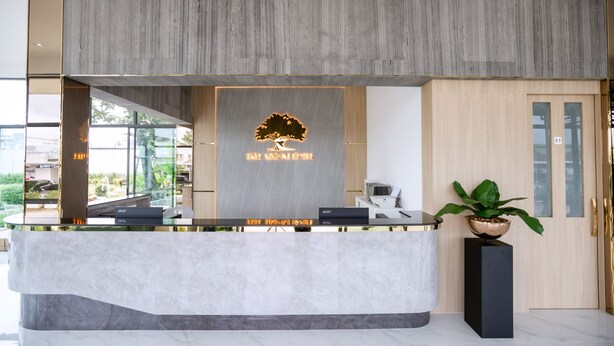 A reception desk with a modern design, featuring a logo and a nameplate. - Tree Airport Hotel Hatyai (Khuan Lang)