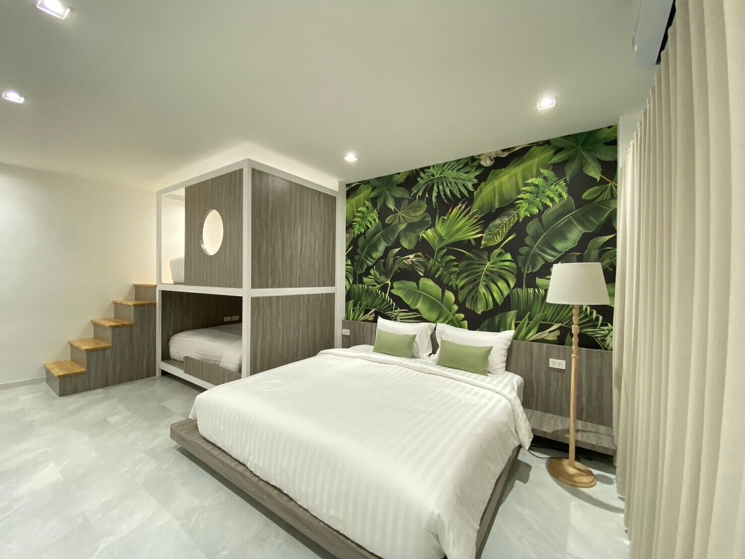 A modern bedroom with a bed, built-in storage, a staircase, and a tropical wallpaper.