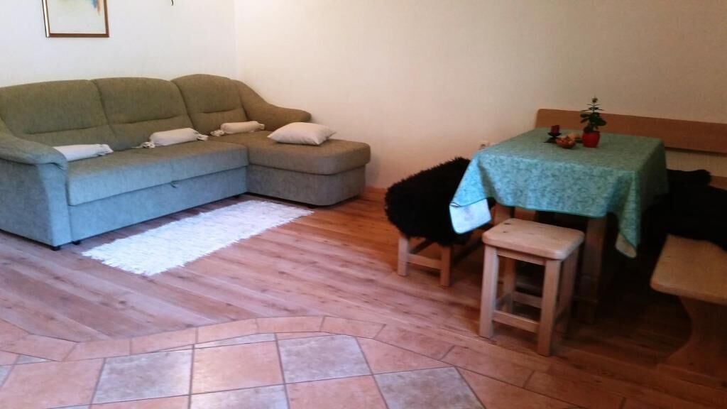 Una sala de estar con un sofá gris, una mesita de madera con mantel verde y piso de baldosas.