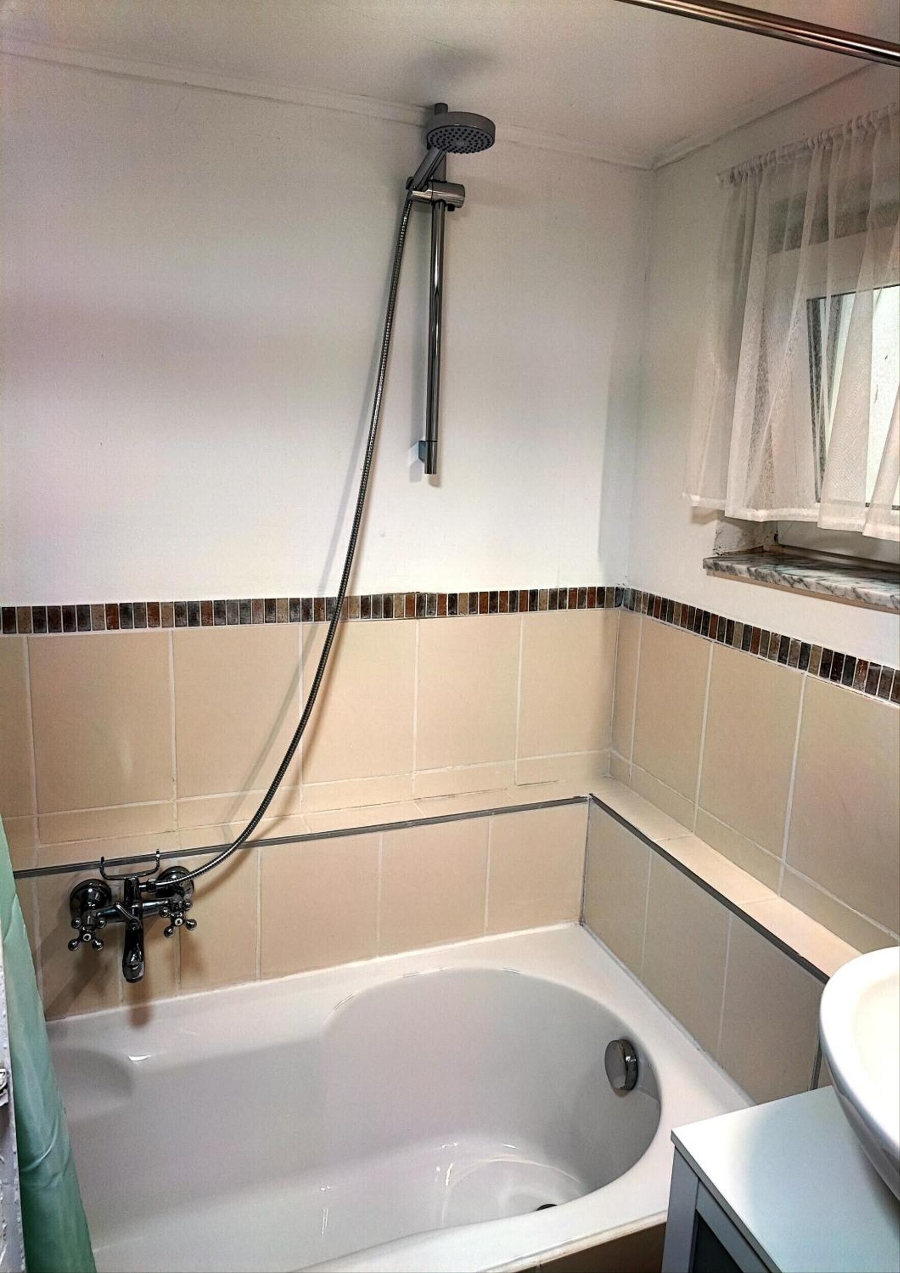 Ein Badezimmer mit einer Badewanne, einer Duschbrause und einem Fenster mit Vorhang.