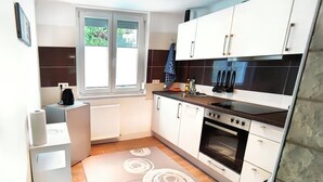 Een compacte keuken met een ingebouwde oven, een koffieapparaat en een raam met zonwering.
