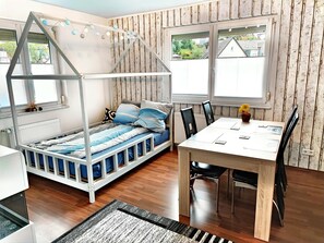 Una habitación con literas, una mesa de comedor con sillas y una ventana con vistas a casas.