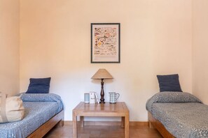 Een kamer met twee bedden, een klein tafeltje met een lamp, een ingelijst foto aan de muur en een tas op het linkerbed.