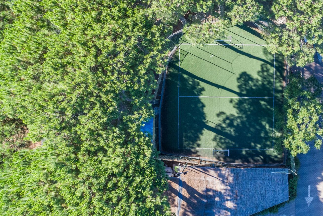 Eine Vogelperspektive auf einen Tennisplatz, der von dichten, grünen Bäumen umgeben ist.