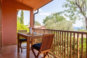 Een balkon met een houten tafel en stoelen, met uitzicht op een schilderachtige omgeving van bomen en een veraf gelegen waterpartij.