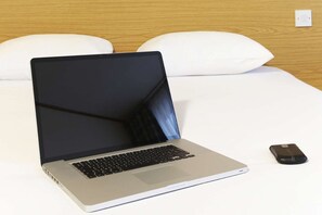 A laptop on a bed with white pillows and a wooden headboard.