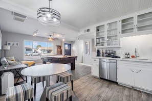 A modern kitchen with white cabinetry, a built-in dishwasher, and a pool table in the living area.