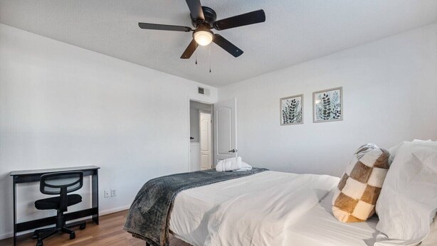 A bedroom with a bed, a desk, a ceiling fan, and two wall art pieces. - Heated Pool | Putting Green | 7 Min Old Town (Scottsdale)
