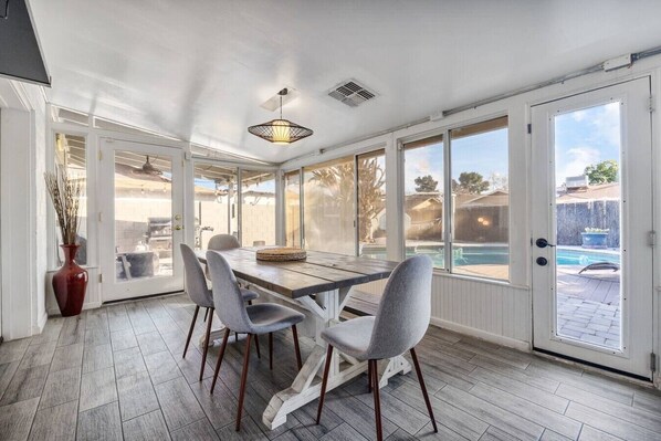 A sunroom with a dining table, chairs, a vase, and a view of a swimming pool.