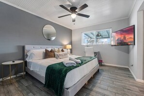 A modern bedroom with a bed, a ceiling fan, a round mirror, a window with blinds, and a painting on the wall. - Heated Pool | Putting Green | 7 Min Old Town (Scottsdale)