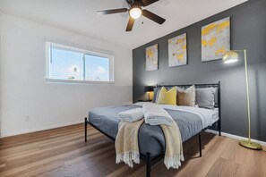 Ein Schlafzimmer mit einem Bett, Deckenventilator, Fenster und Bildern an der Wand.