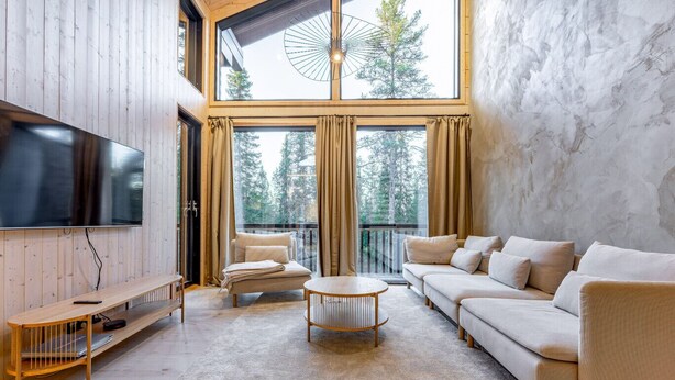 Un salon moderne doté d’un grand téléviseur à écran plat, d’un canapé, d’une table basse et d’un balcon offrant une vue sur les arbres.