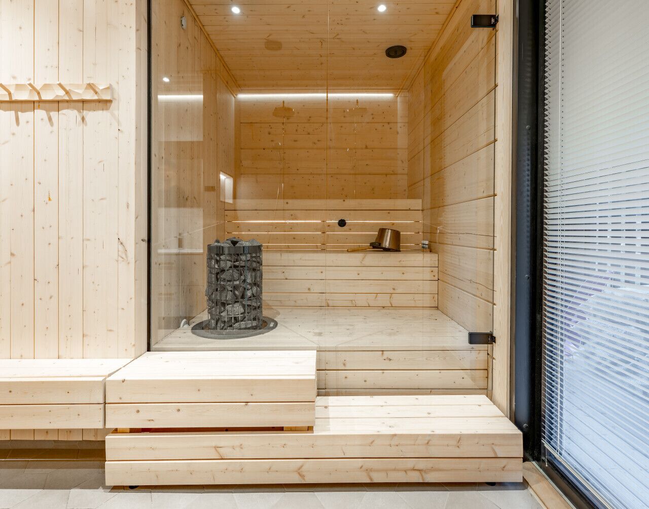 Uma sala de sauna com paredes e bancos de madeira, um aquecedor de pedra e uma janela com persianas.