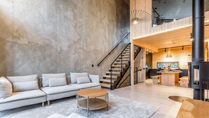 Un vaste espace de vie agrémenté d’un canapé moderne, d’une table basse en bois et d’un escalier menant à l’étage supérieur.