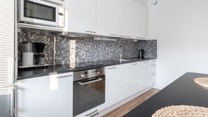 A modern kitchen with white cabinets, a black countertop, a microwave, a coffee maker, and a black kettle. - Bright & Cozy 1BR Home near Downtown (Lahti)