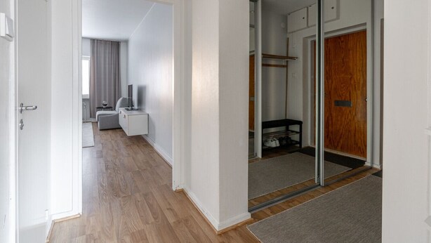 A hallway with a wooden floor, a grey sofa, a white cabinet, and a sliding glass door leading to a room with a wooden door and a shoe rack. - Bright & Cozy 1BR Home near Downtown (Lahti)